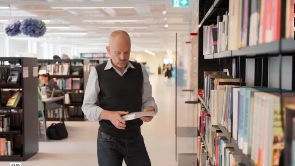 Studerende på uddannelse til pædagogisk assistent står foran bogreol og læser i en bog