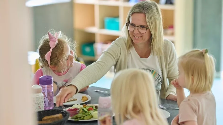 Pædagogisk assistent sidder med tre børnehavebørn omkring et bord
